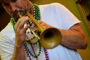 Photo of Rob Alley playing the trumpet while wearing Mardi Gras beads