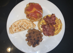 Mini pizza, mini quesadilla, eggs and bacon, and a cookie all made in a waffle maker on a plate