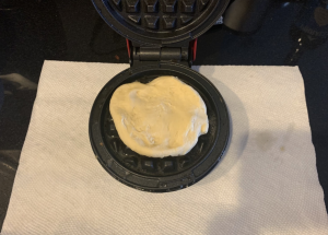 Crescent roll dough cooking on waffle maker.