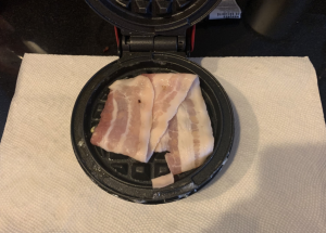 Uncooked bacon cooking on a waffle maker